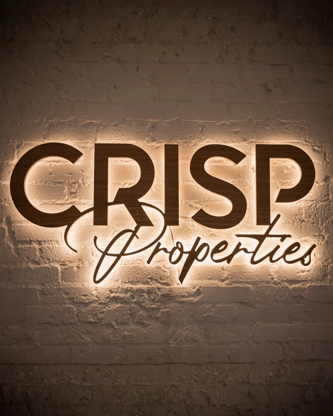 The Crisp Properties sign lit up on a brick wall